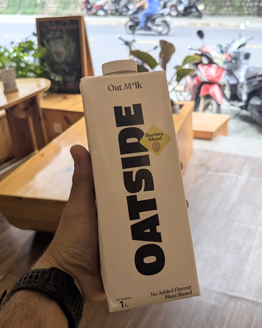 Hộp sữa yến mạch Oatside trên tay, phía sau là không gian quán